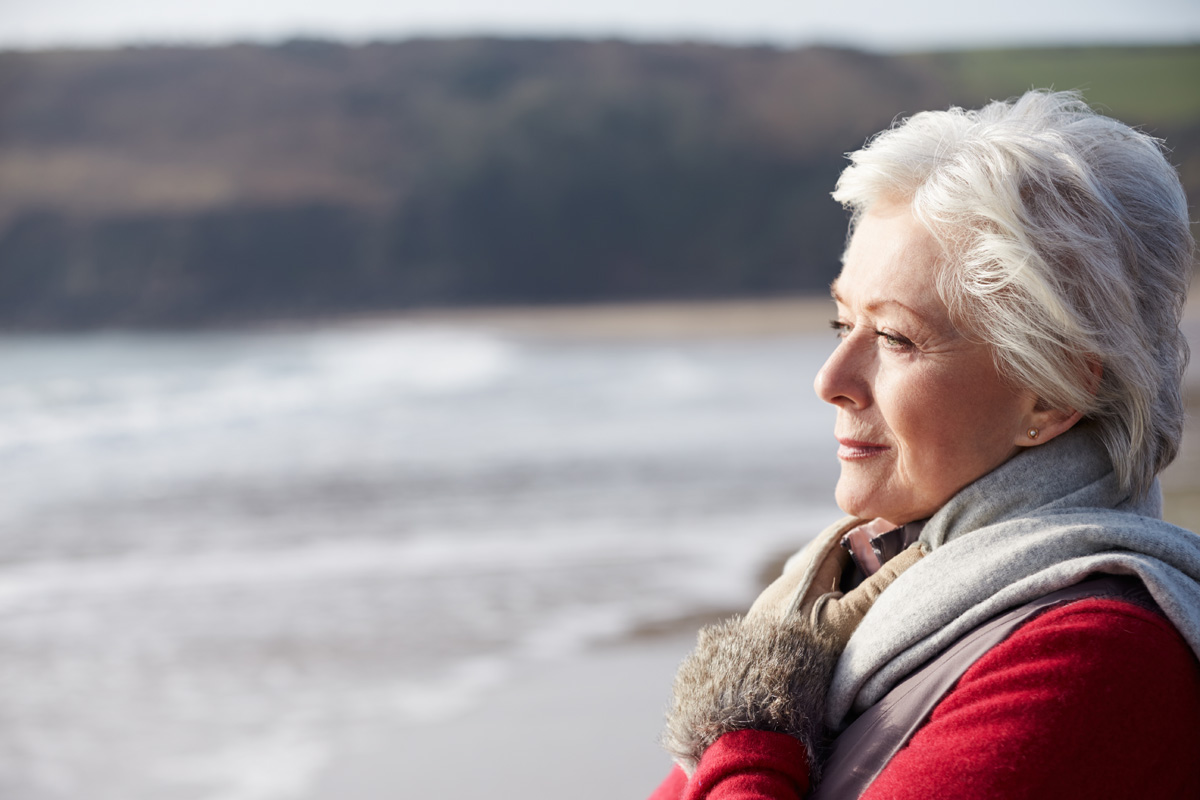 Senior Woman Walking On Winter Beach Looking Off Camera