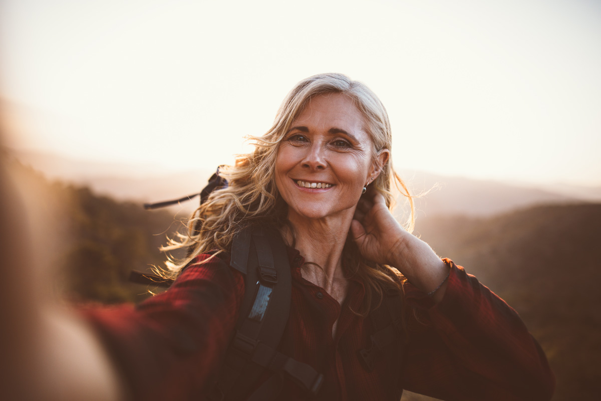 Cheerful senior woman on hiking trip on the mountains taking a selfie on mountain top